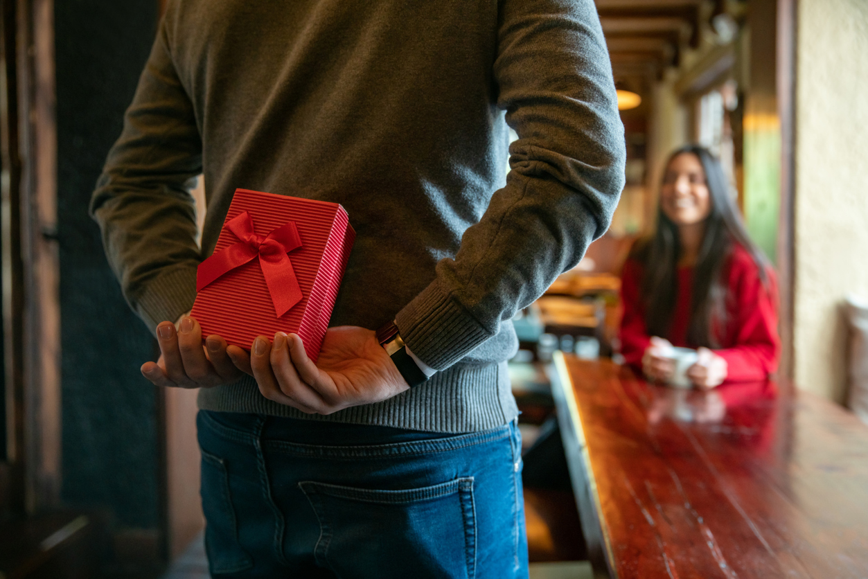 Man surprising woman with a gift while celebrating Valentines at a restaurant